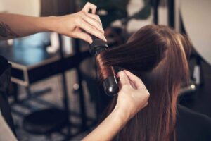 A person using a dropper to apply hair serum to the tips of their long brown hair.