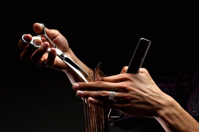 A person examining their hair in a well-lit bathroom mirror with visible strands in their hand.